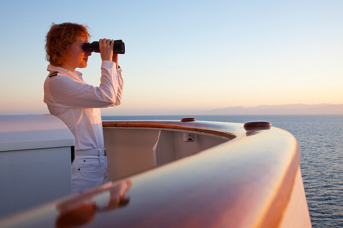Safety Officer Claudia Kempkes with binoculars on the bridge nook of cruise ship MS Deutschland (Reederei Peter Deilmann) at sunset, Gulf of California, near Mexico