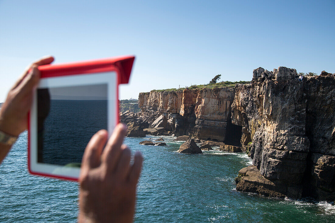 Mann fotografiert die Felsformation Boca do Inferno Höllenmund mit iPad, Cascais, nahe Lissabon, Portugal