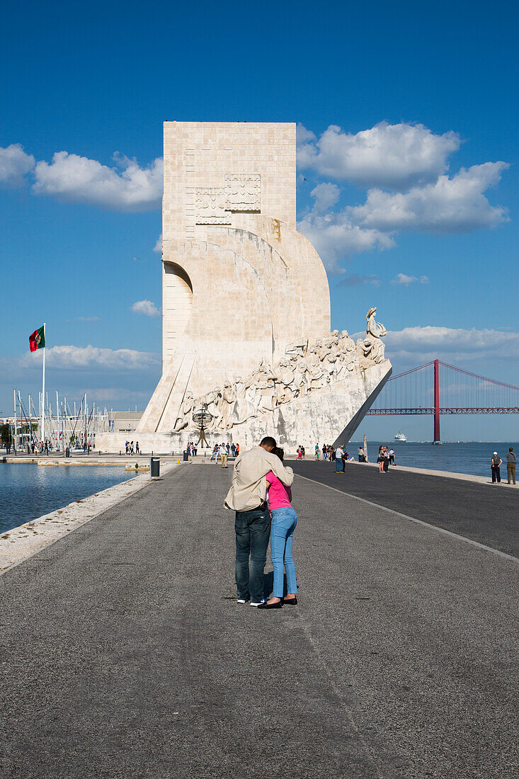 Couple at the Padrao dos Descobrimentos (Discoveries Monument) in Belem with Ponte 25 de Abril bridge over Tagus river, Lisbon, Lisboa, Portugal