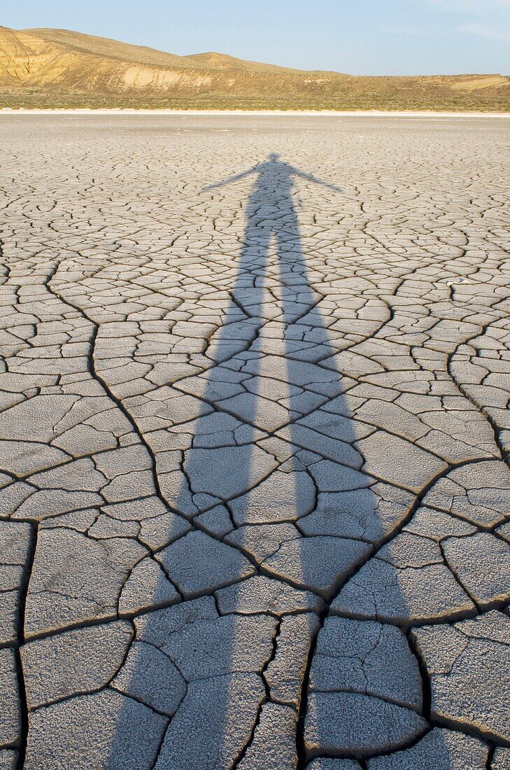 Silhouette of person on patterns of cracked mud on dry lakebed of Harney Lake, Malheur National Wildlife Refuge, Oregon
