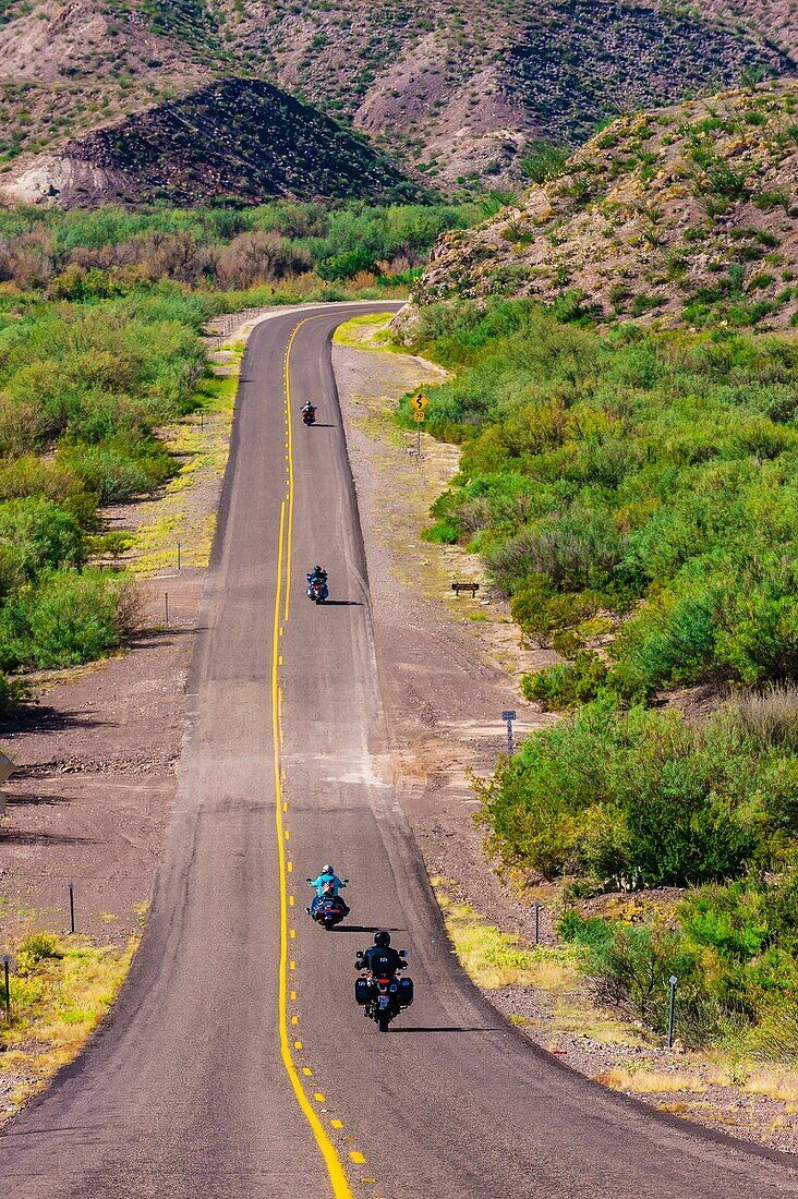 Motoryclists ride down a long straight road FM 170, the Camino del Rio, Big Bend Ranch State Park, Texas USA