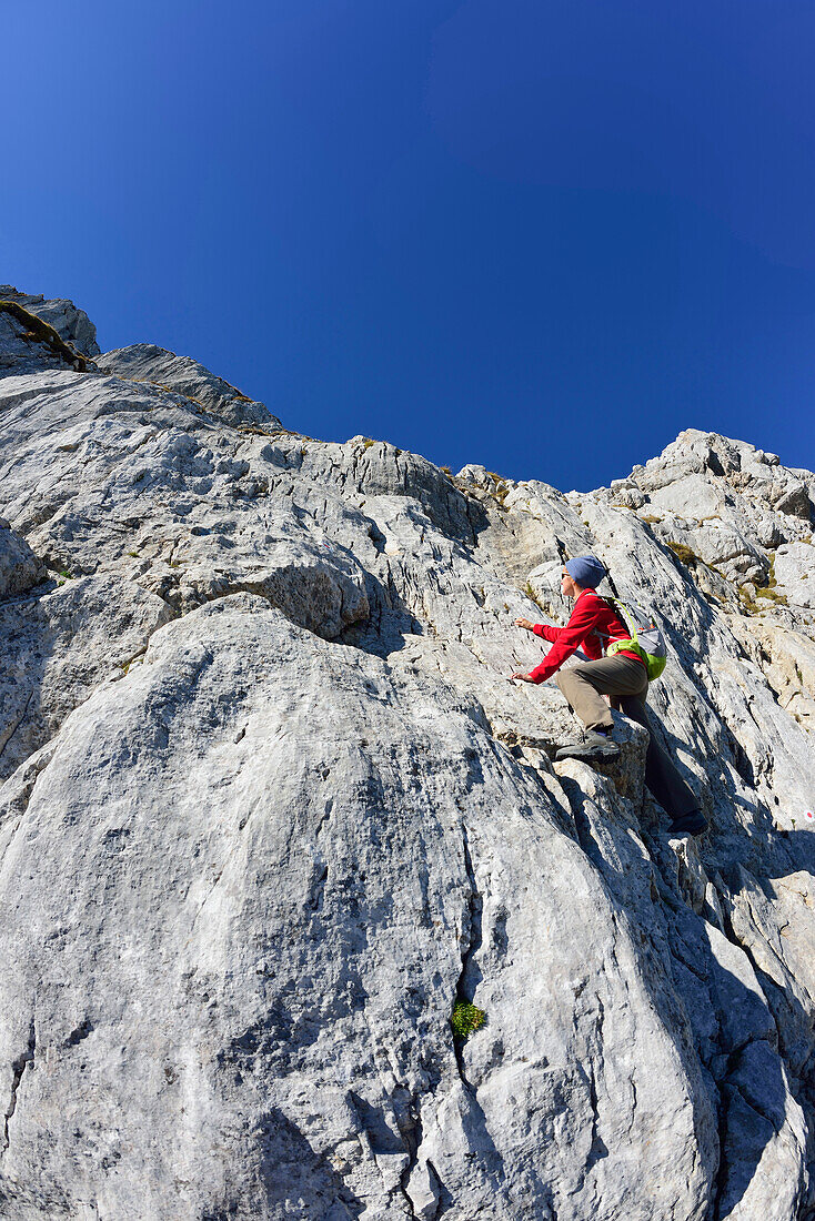 Woman climbing over rock to Hochkalter, Berchtesgaden National Park, Berchtesgaden Alps, Upper Bavaria, Bavaria, Germany