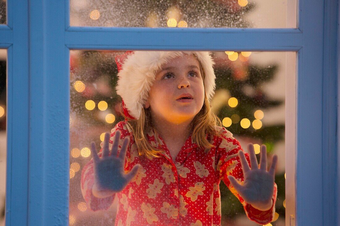 Junges Mädchen, das aus dem Fenster schaut und auf den Weihnachtsmann wartet