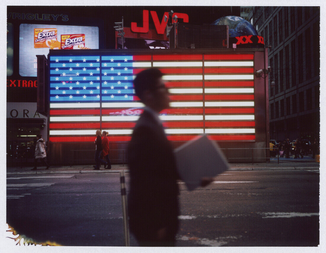 Businessman Walking in Front of Neon American Flag, Times Square, New York City, USA