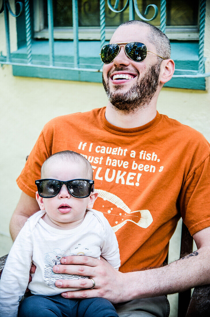 Bearded Father with Sunglasses Smiling and Holding Infant Son Wearing Sunglasses, Outside