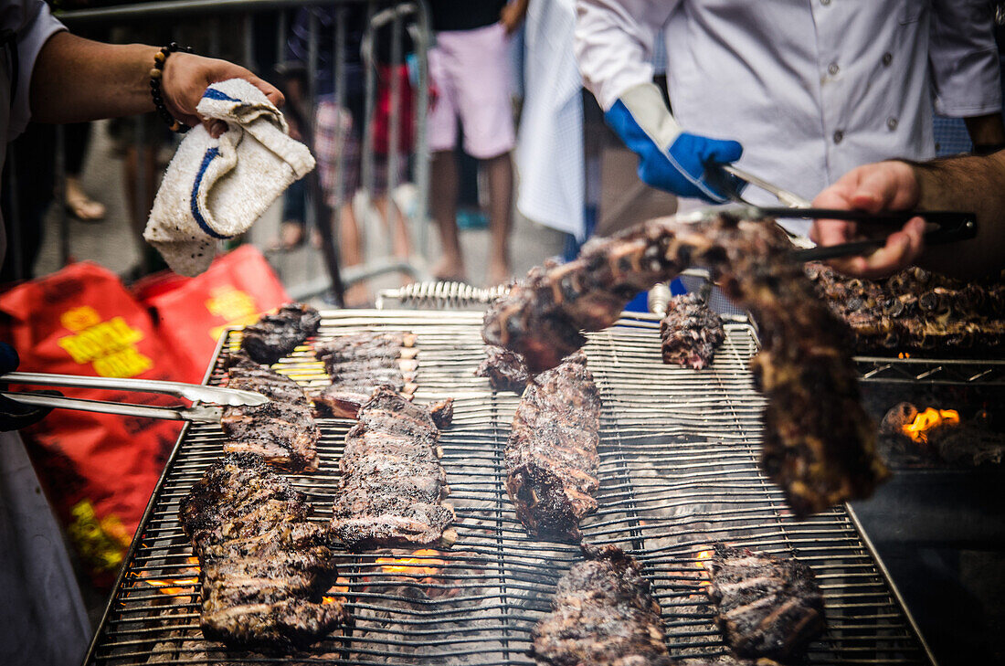 Cooks with Tongs Attending to Barbecue Ribs on the Grill