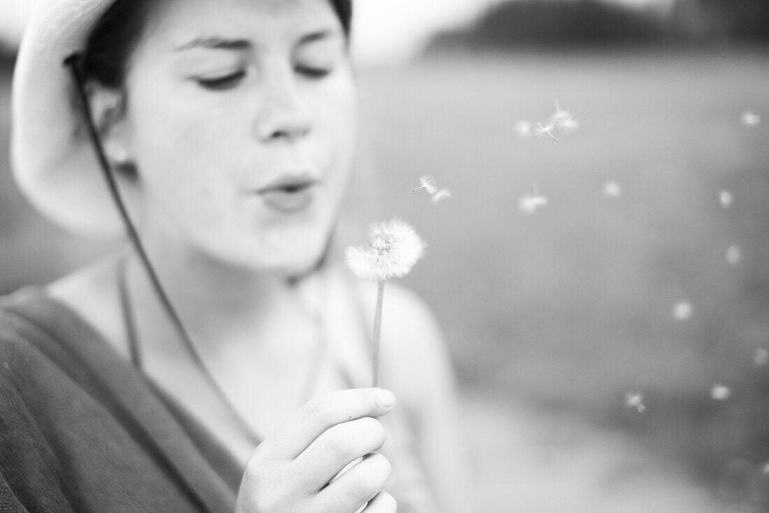 Young Woman Blowing on Dandelion