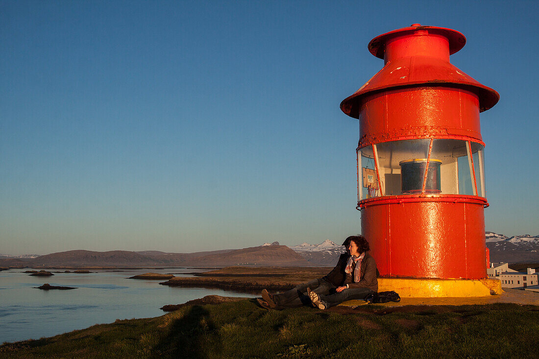 Couple Leaning Against The Stykkisholmur Lighthouse Looking At The Midnight Sun, Snaefellness Peninsula, Western Iceland