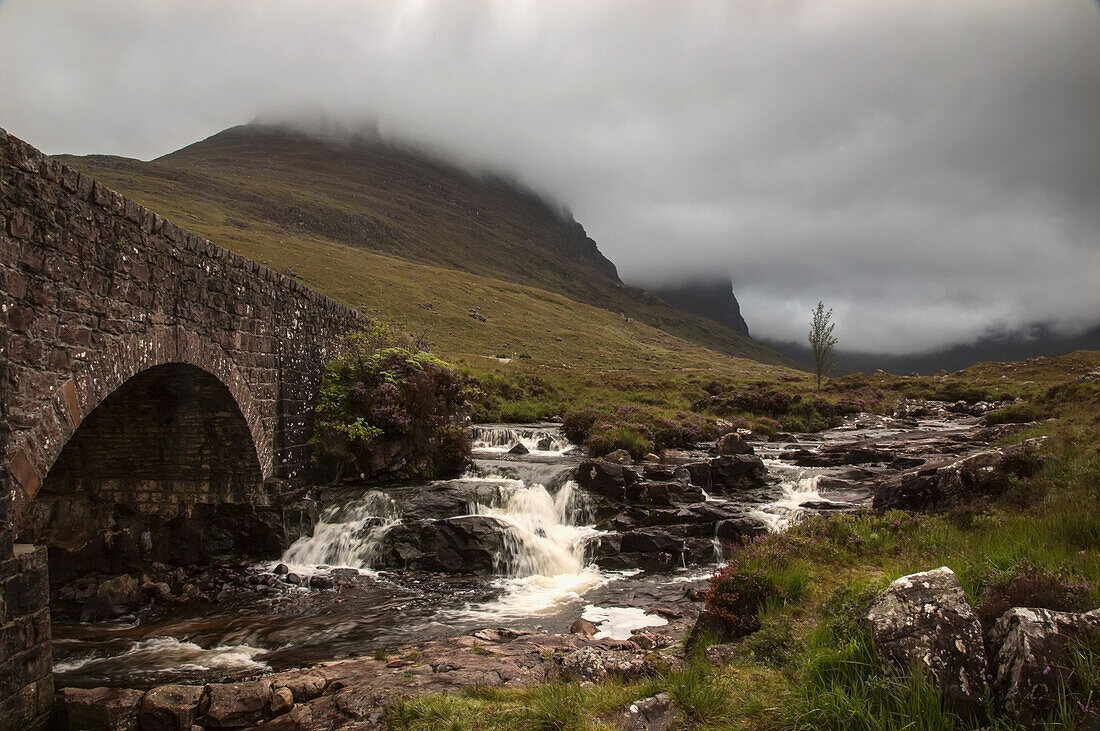 'Low Clouds Over A Landscape With A Stream Cascading Over Rocks And Under A Bridge; Applecross Peninsula Scotland'