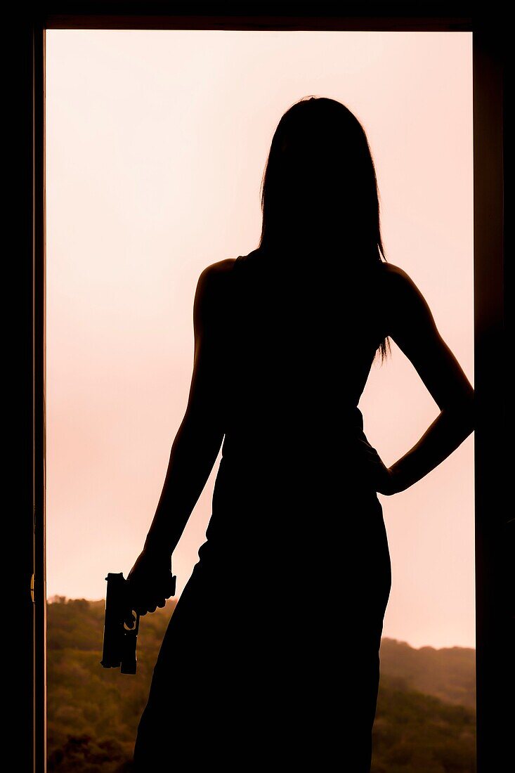 Silhouette of a woman holding a gun while standing in a door frame