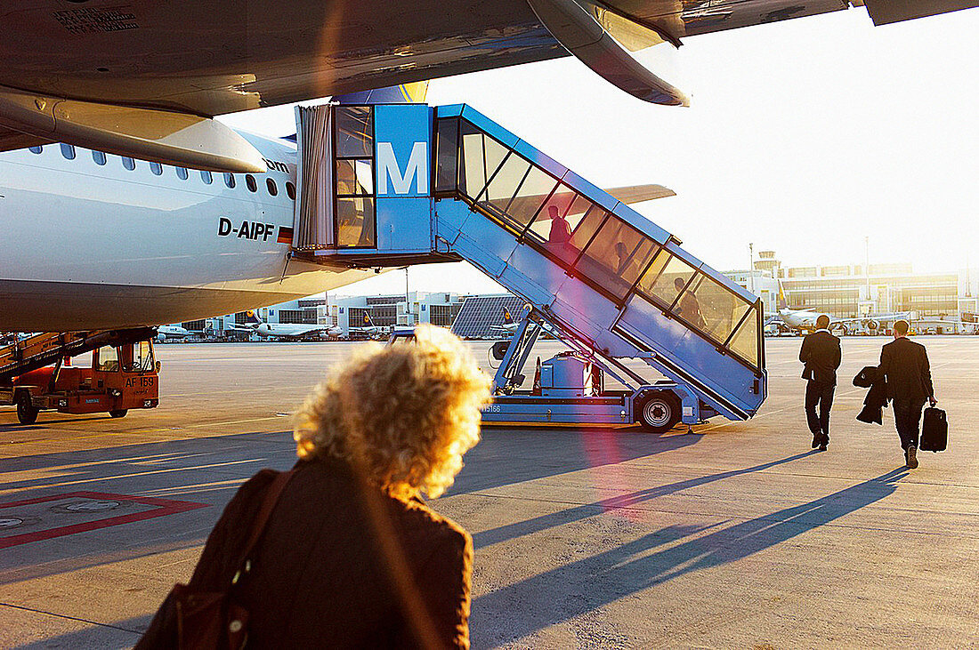 Businessmen and travelers board a plane on the tarmac at sunset