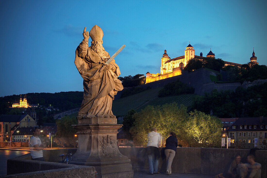 Heiligenstatue auf Alter Mainbrücke mit Blick auf Festung Marienberg bei Nacht, Würzburg, Franken, Deutschland