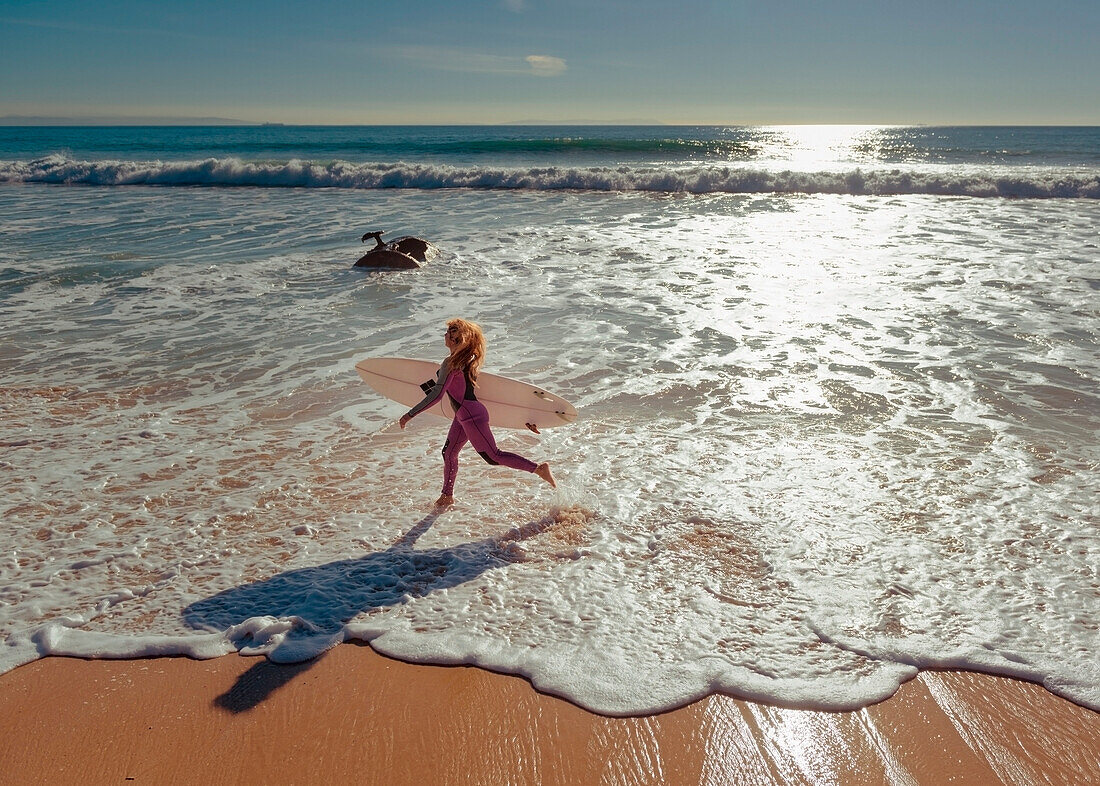 Woman in wetsuit running on beach, Tarifa, Costa de la Luz, Cadiz, Andalusia, Spain