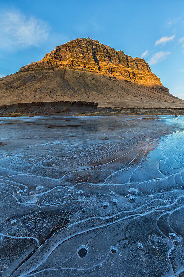 Sunrise light hitting the mountain Kirkjufell with the ice from a frozen pond in the foreground, Snaefellsnes Peninsula, Iceland