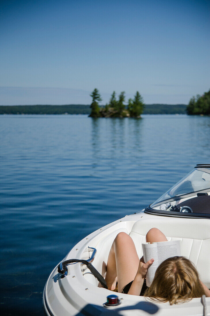 Young Woman Sitting in Boat on Lake Reading Book