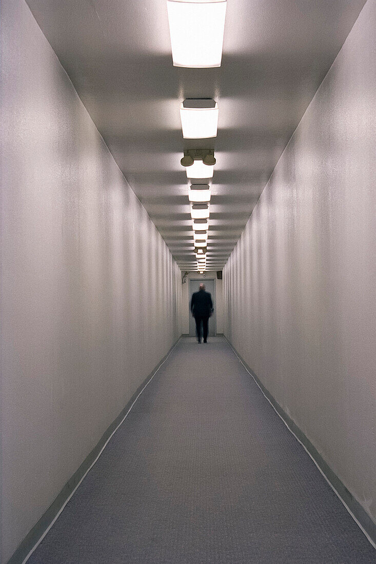 Man Standing at end of Long Hallway, Rear View