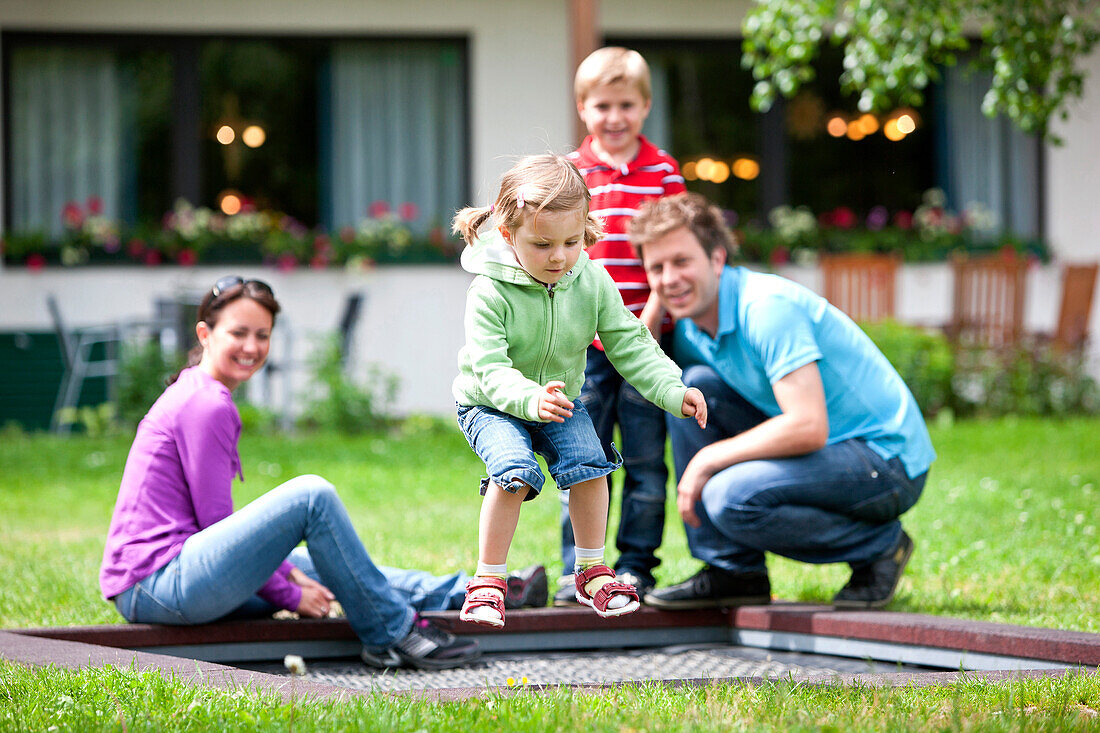 Mädchen springt auf einem Trampolin, Familie im Hintergrund, Steiermark, Österreich