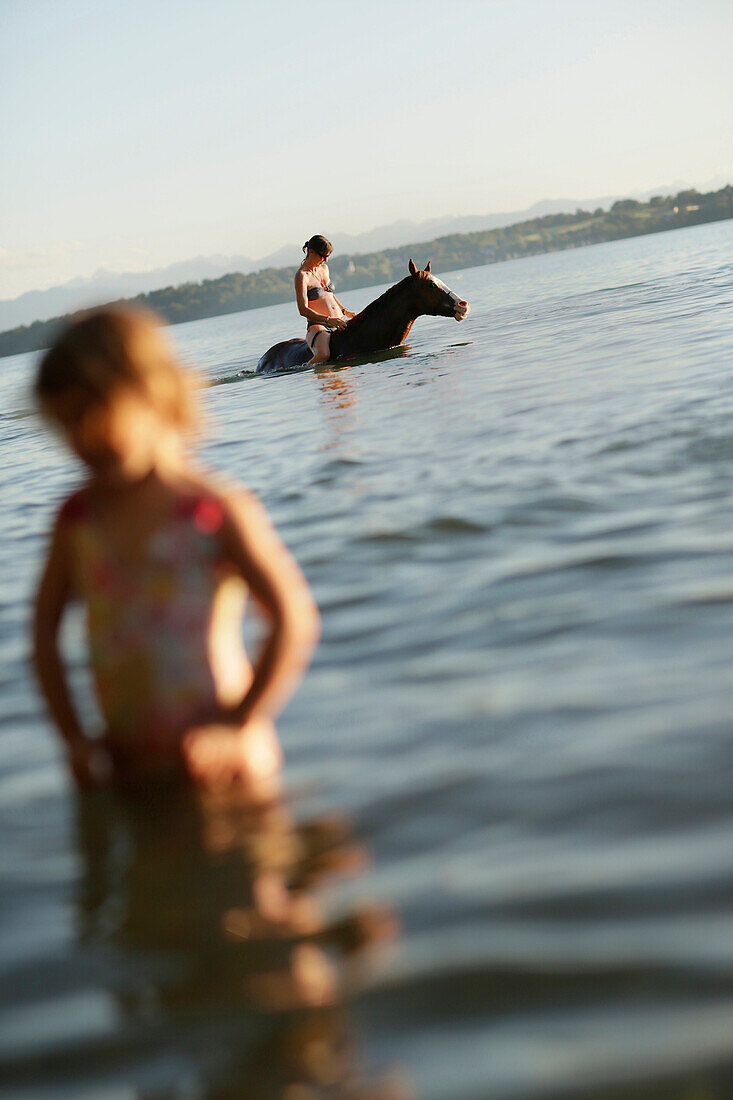 Frau reitet auf einem Pferd im Starnberger See, Mädchen im Vordergrund, Ammerland, Münsing, Oberbayern, Bayern, Deutschland