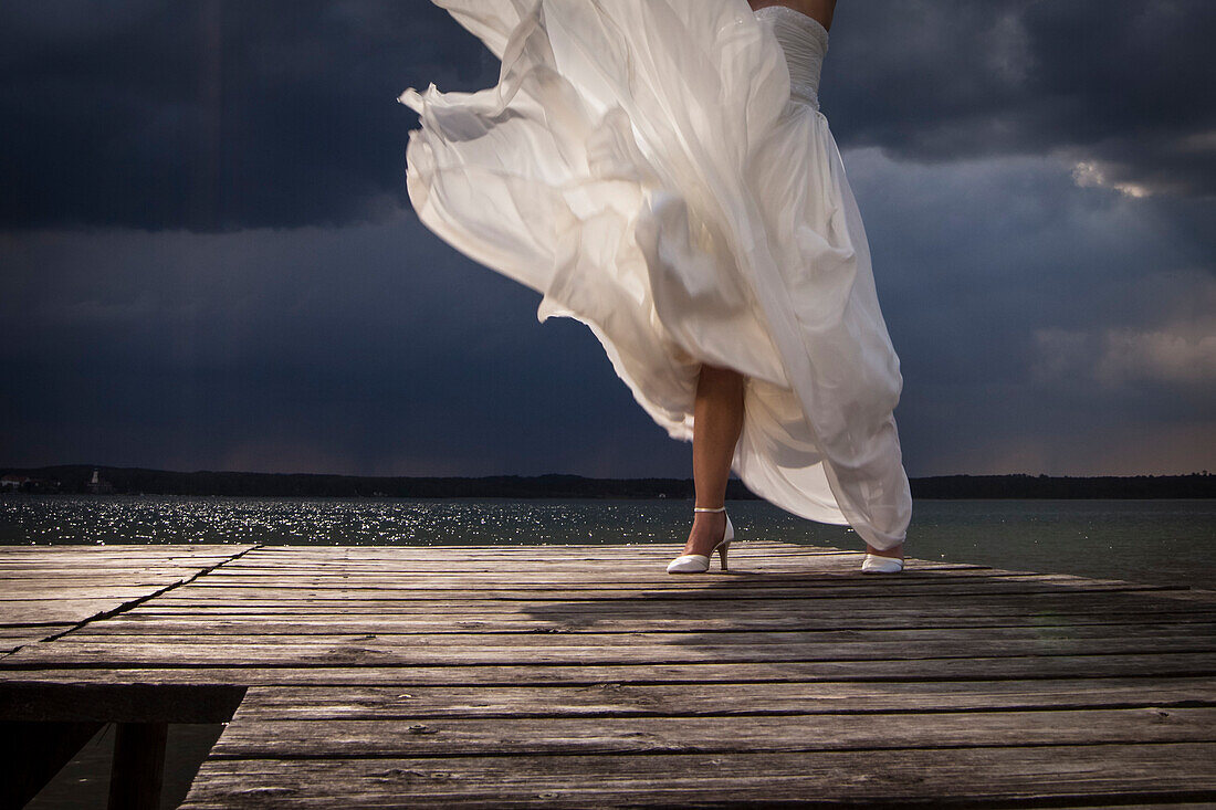 Bride standing on a jetty in front of thunderclouds, Lake Starnberg, Bavaria, Germany