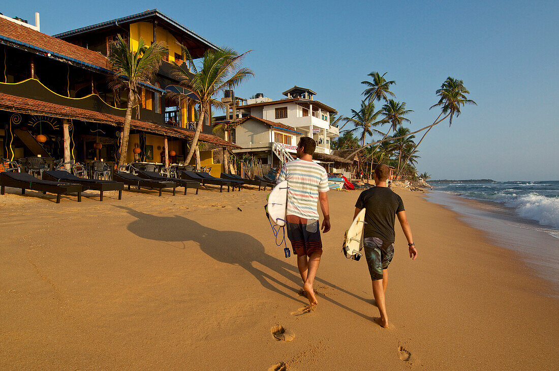 Zwei Surfer tragen ihre Surfboards am Strand von Hikkaduwa, Hikkaduwa, Südwestküste, Sri Lanka, Südasien