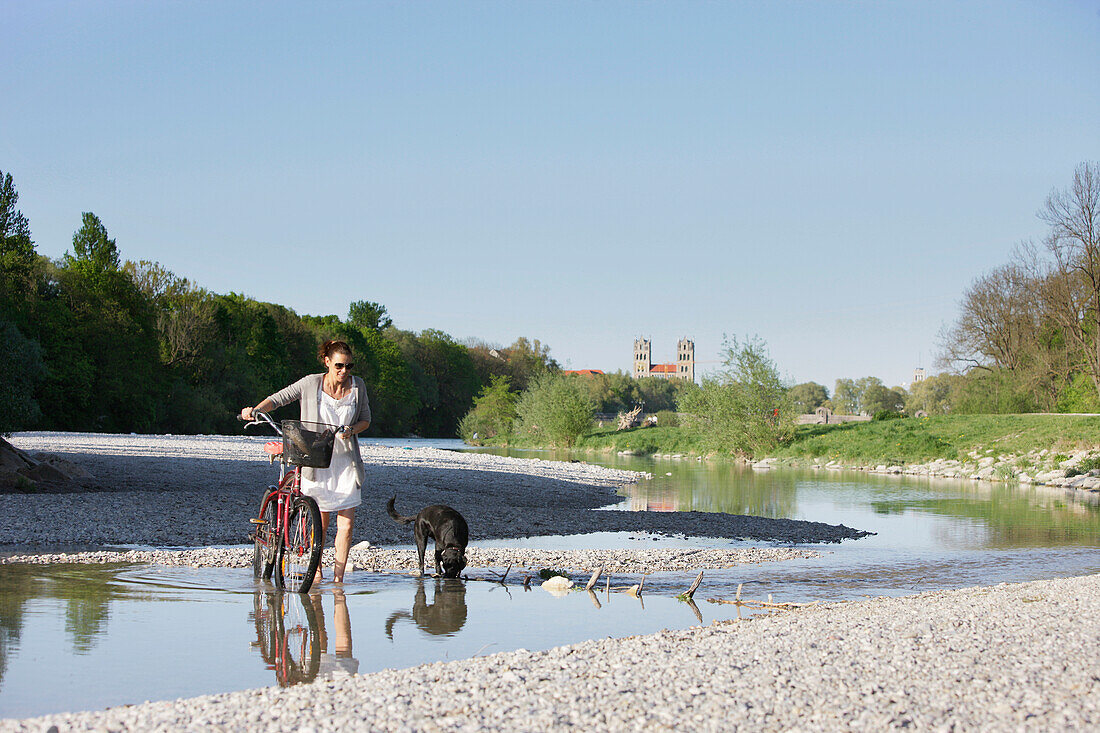 Fahrradfahrerin mit Hund auf einer Kiesbank an der Isar, München, Bayern, Deutschland