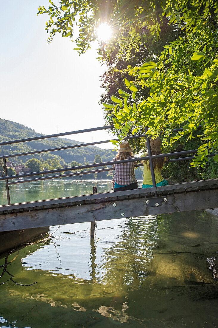 Zwei junge Frauen sitzen auf einem Steg am Rhein, Rheinfelden, Baden-Württemberg, Deutschland