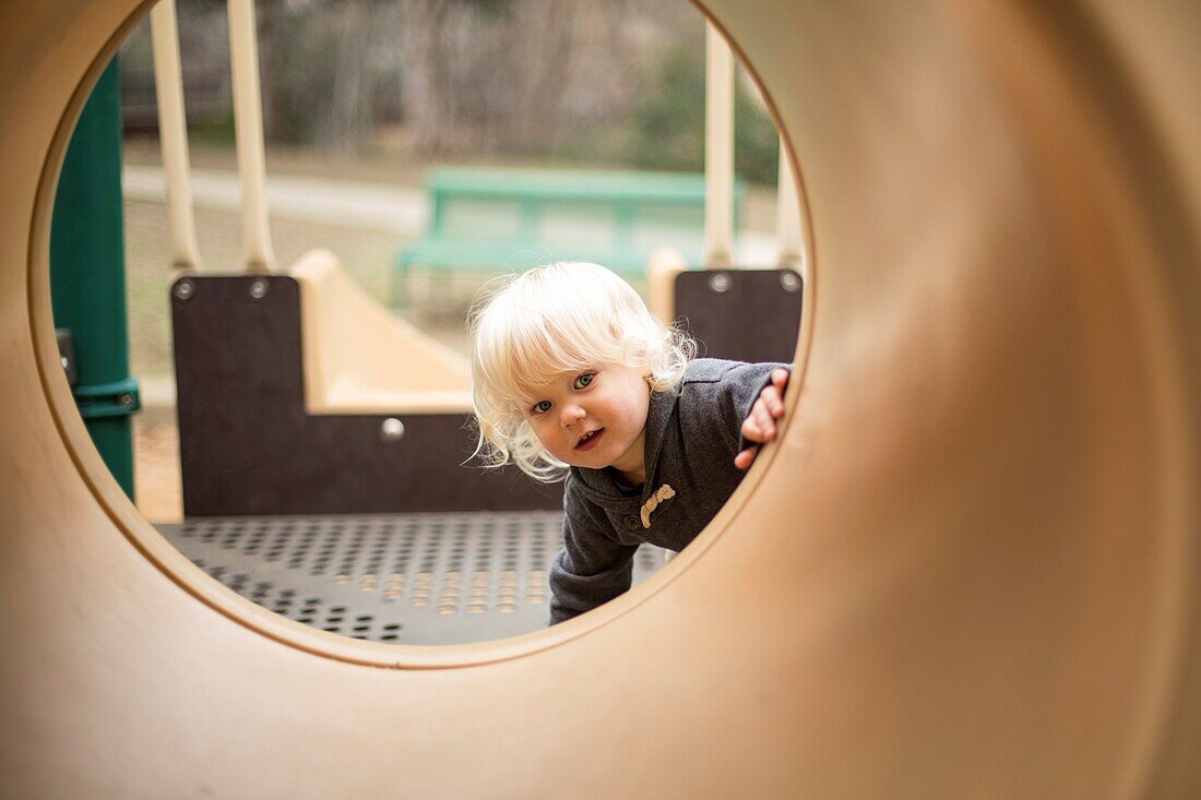 Young boy looking through pipe on playground