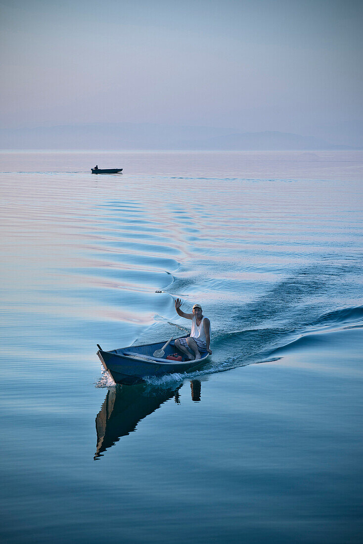 Fisherman in boat waving to the camera, Murici, Lake Skadar National Park, Montenegro, Western Balkan, Europe