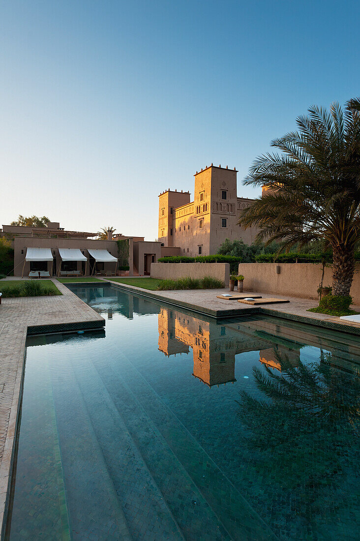 Swimming pool of Dar Ahlam Hotel with main kasbah in background at dawn, Skoura, Morocco