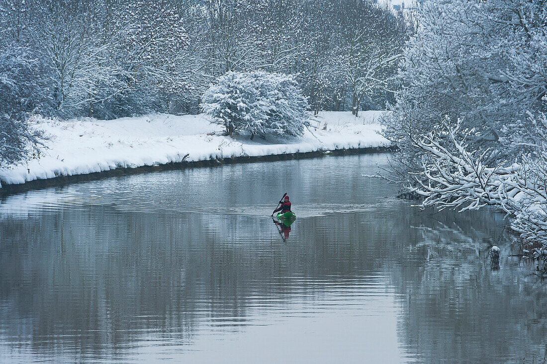Canoeist going down River Ouse in snowy conditions, Lewes, East Sussex, UK