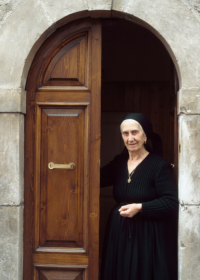 Lady In Traditional Dress Standing In The Doorway Of Her House, Scanno, Abruzzo, Italy.