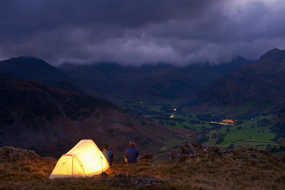 Lit tent on hill above Langdale on stormy evening, Lake District, Cumbria, England