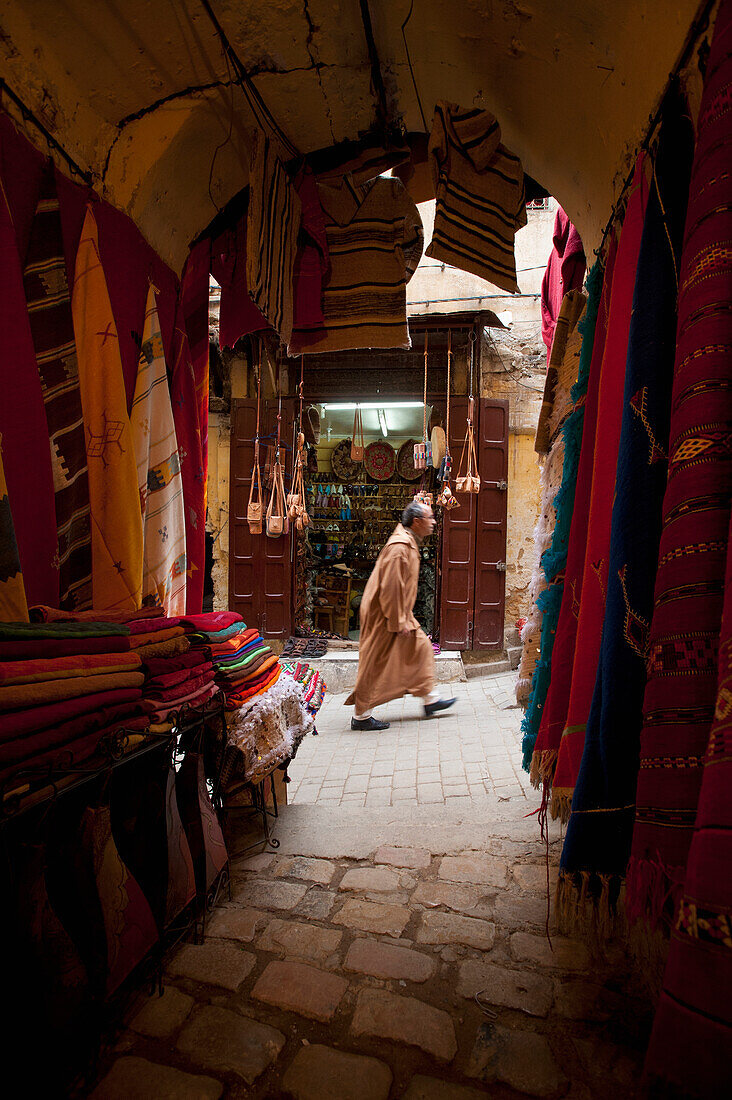 Looking past clothes for sale in narrow passageway to man walking up alley, Fez, Morocco