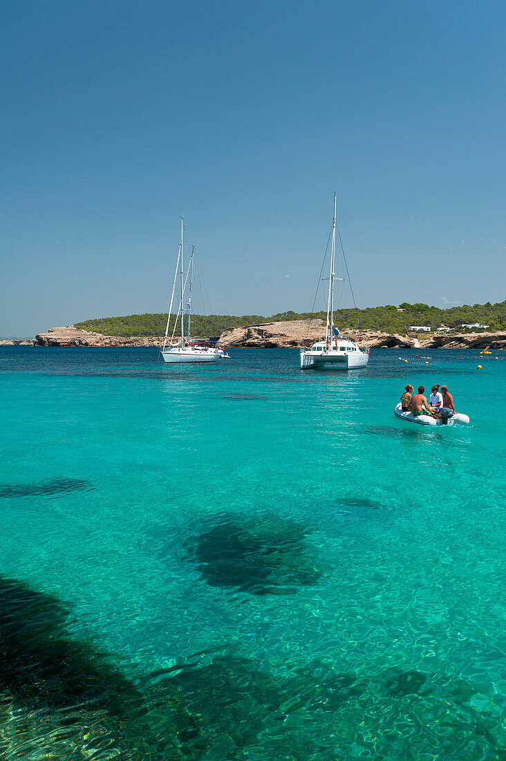 People in small boat going out to their yacht off Cala Bassa Beach, Ibiza, Spain