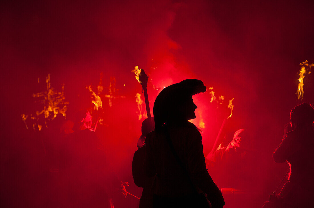 Silhouette of pirate with burning torch from Southover Bonfire Society lit by red flares on United Grand Procession down High Street, Bonfire Night, Lewes, East Sussex, England, UK