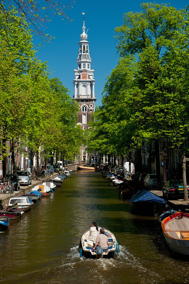 Couple in boat going along canal with spire of Zuiderkerk Church in background, Amsterdam, Holland