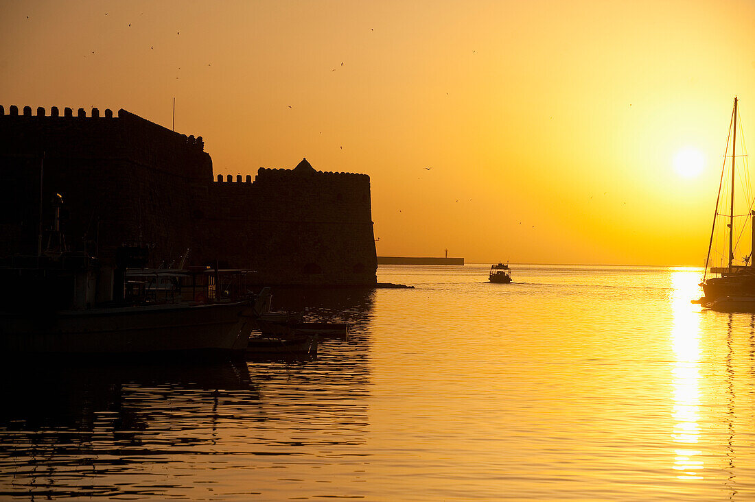 Fishing boat, harbor and Venetian fortress at dawn, Heraklion, Crete, Greece