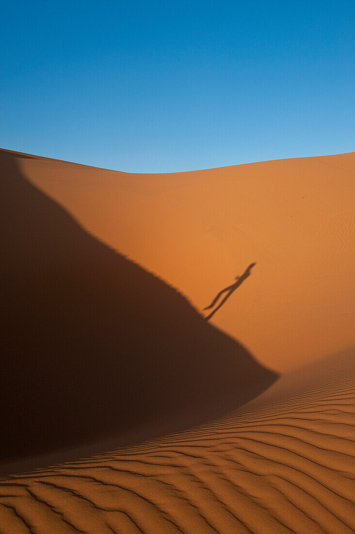 Shadow of man running up sand dune in Erg Chebbi near Merzouga, Sahara Desert, Morocco