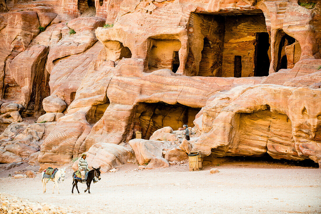 Mann reitet auf einem Esel vor Höhlengräbern, Petra, Jordanien, Naher Osten