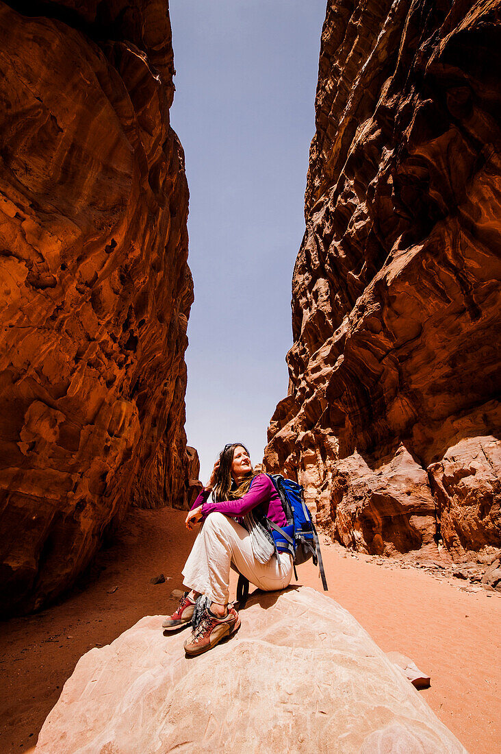 Frau rastet auf einem Stein in einer Felsenschlucht, Wadi Rum, Jordanien, Naher Osten