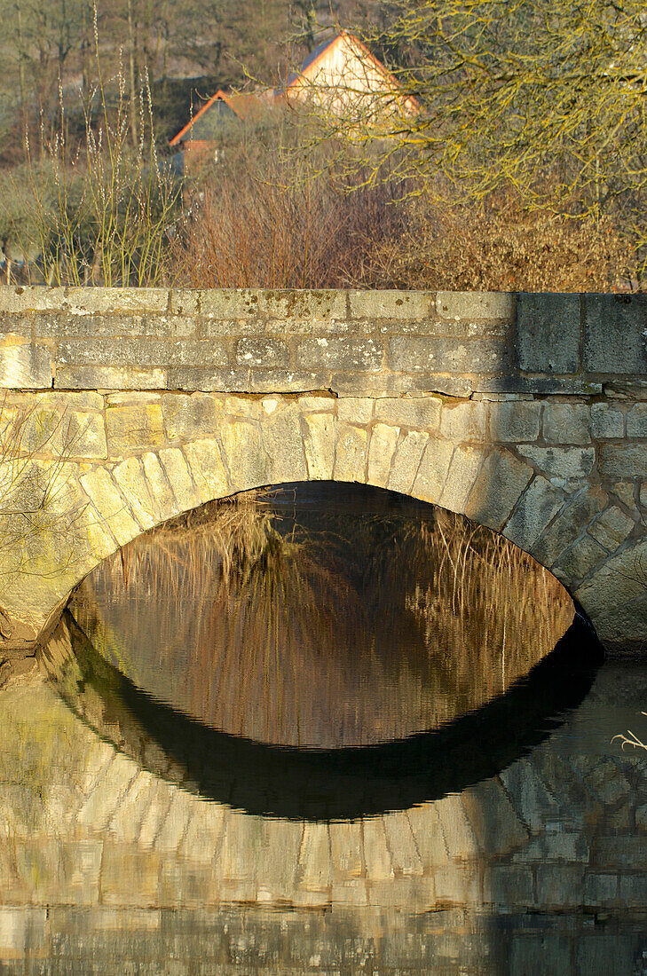 Old stone bridge with reflection at Salzboeden over the small river Salzboede near Giessen, Hesse, Germany