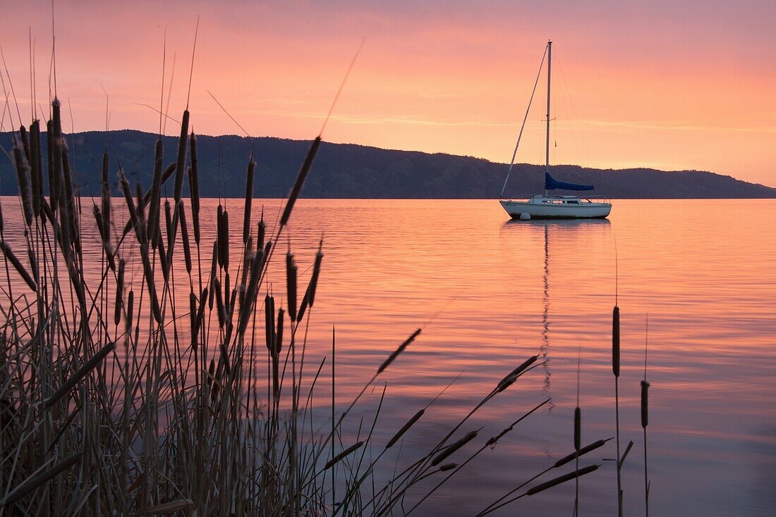 A sailboat is reflected in the dawn glow on California's Clear Lake.