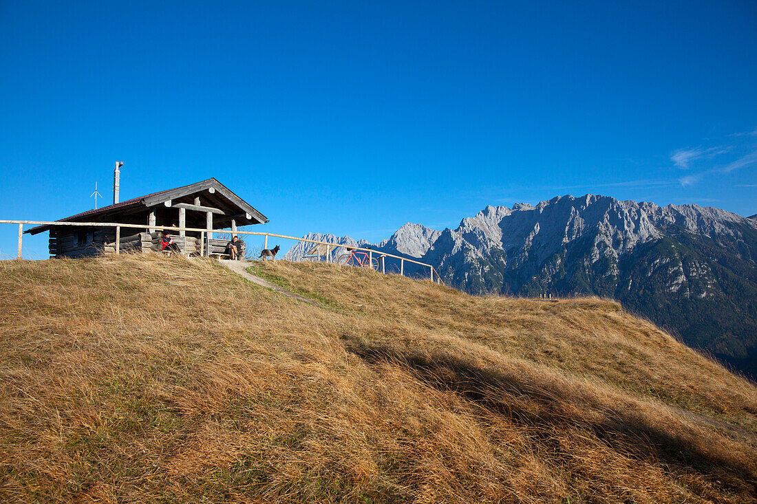 Wanderer bei der Rast an der Gipfelhütte auf dem Hohen Kranzberg, Blick zum Karwendelgebirge, bei Mittenwald, Bayern, Deutschland