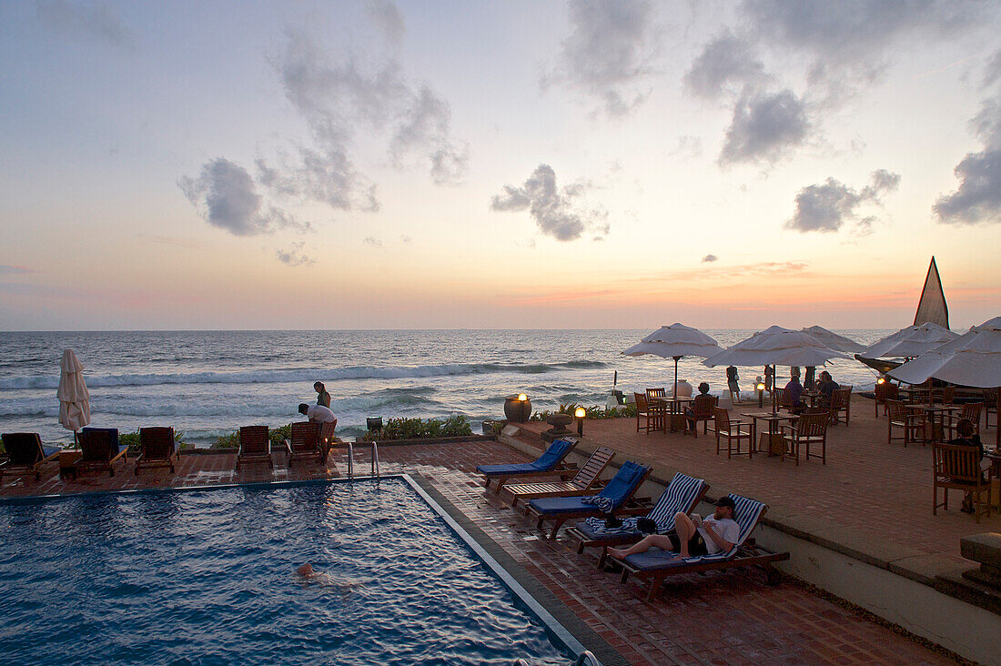 Pool direkt am Meer kurz nach Sonnenuntergang und Besucher am Pool des Galle Face Hotel, Colombo, Sri Lanka