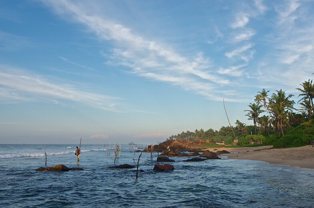 Stilt fishermen in the early morning in front of a rocky coastline near Weligama, South Sri Lanka