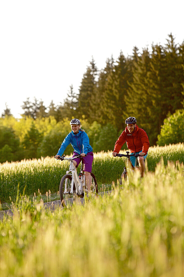 Two cyclists riding electric bicycles between fields, Tanna, Thuringia, Germany