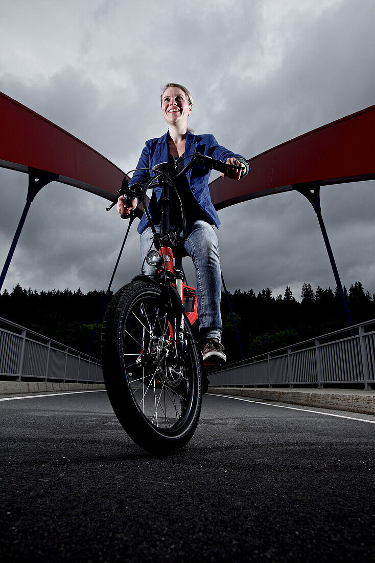 Woman riding an electric bicycle passing a bridge, Tanna, Thuringia, Germany