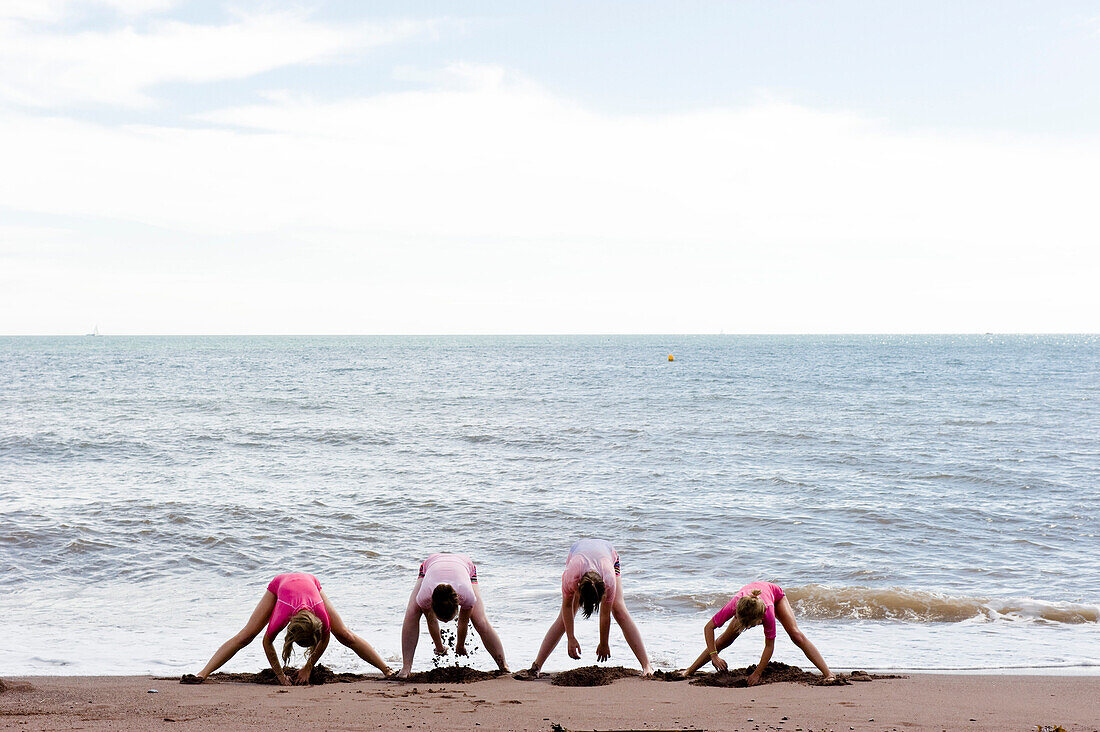 Vier Personen buddeln am Strand, Teignmouth, Devon, South West England, England, Großbritannien