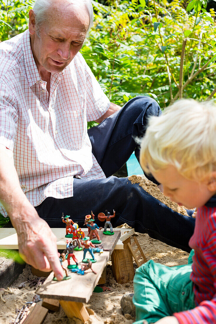 Junge (3 Jahre) und Großvater spielen mit Figuren in einem Sandkasten, Freital, Sachsen, Deutschland