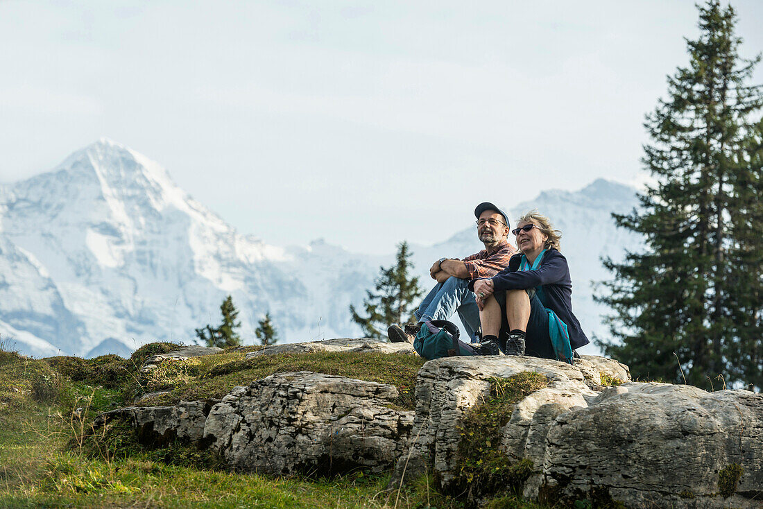 Couple resting on a rock, Eiger, Moench and Jungfrau in background, Beatenberg, Bernese Oberland, Canton of Bern, Switzerland